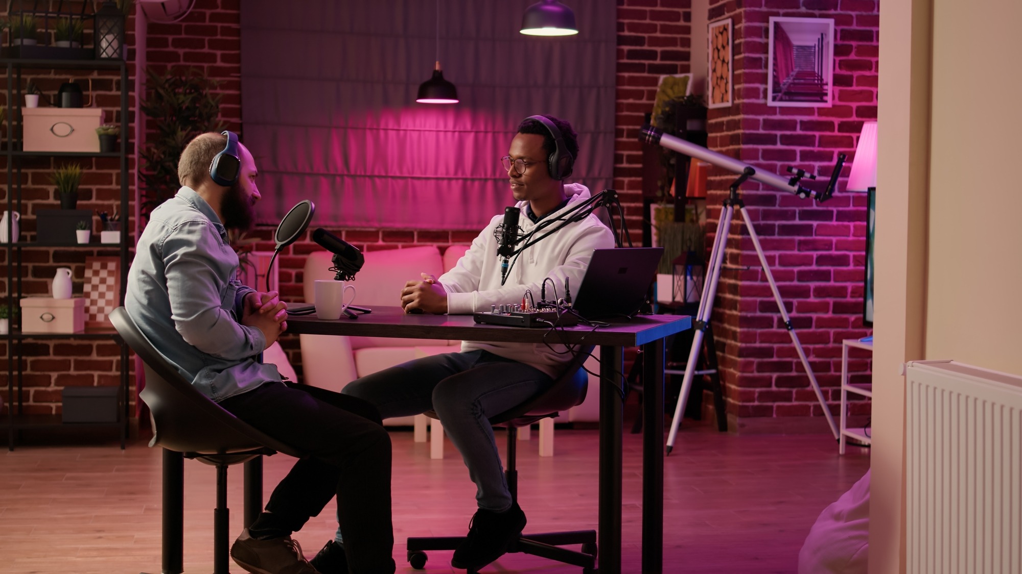 African american podcaster greeting guest doing fist bump hand gesture while recording podcast using digital video camera in home studio. Internet radio host in interview with famous influencer.