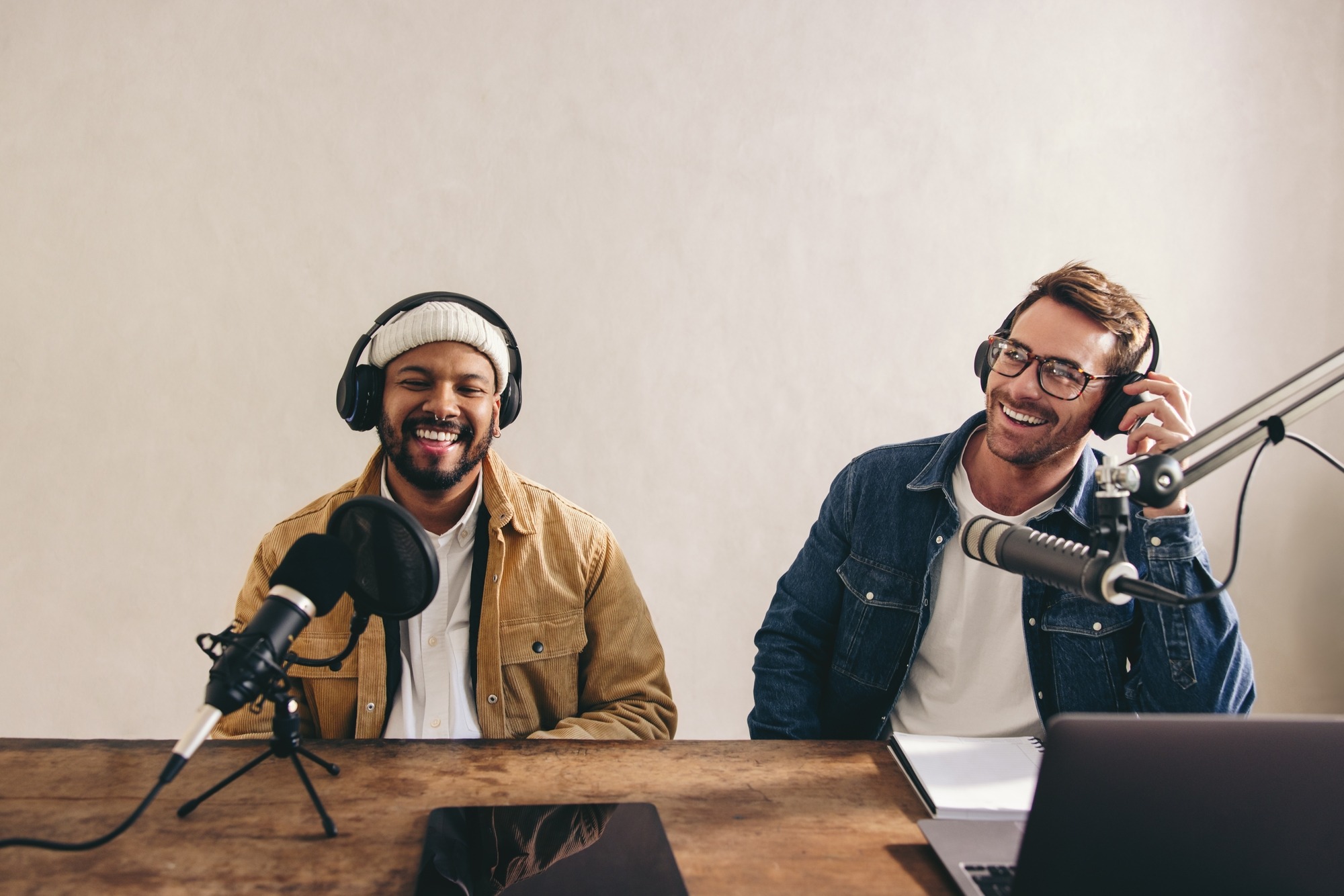 Two happy radio presenters having a good time on air. Young men smiling happily while recording an audio broadcast in a studio. Cheerful content creators co-hosting an internet podcast.
