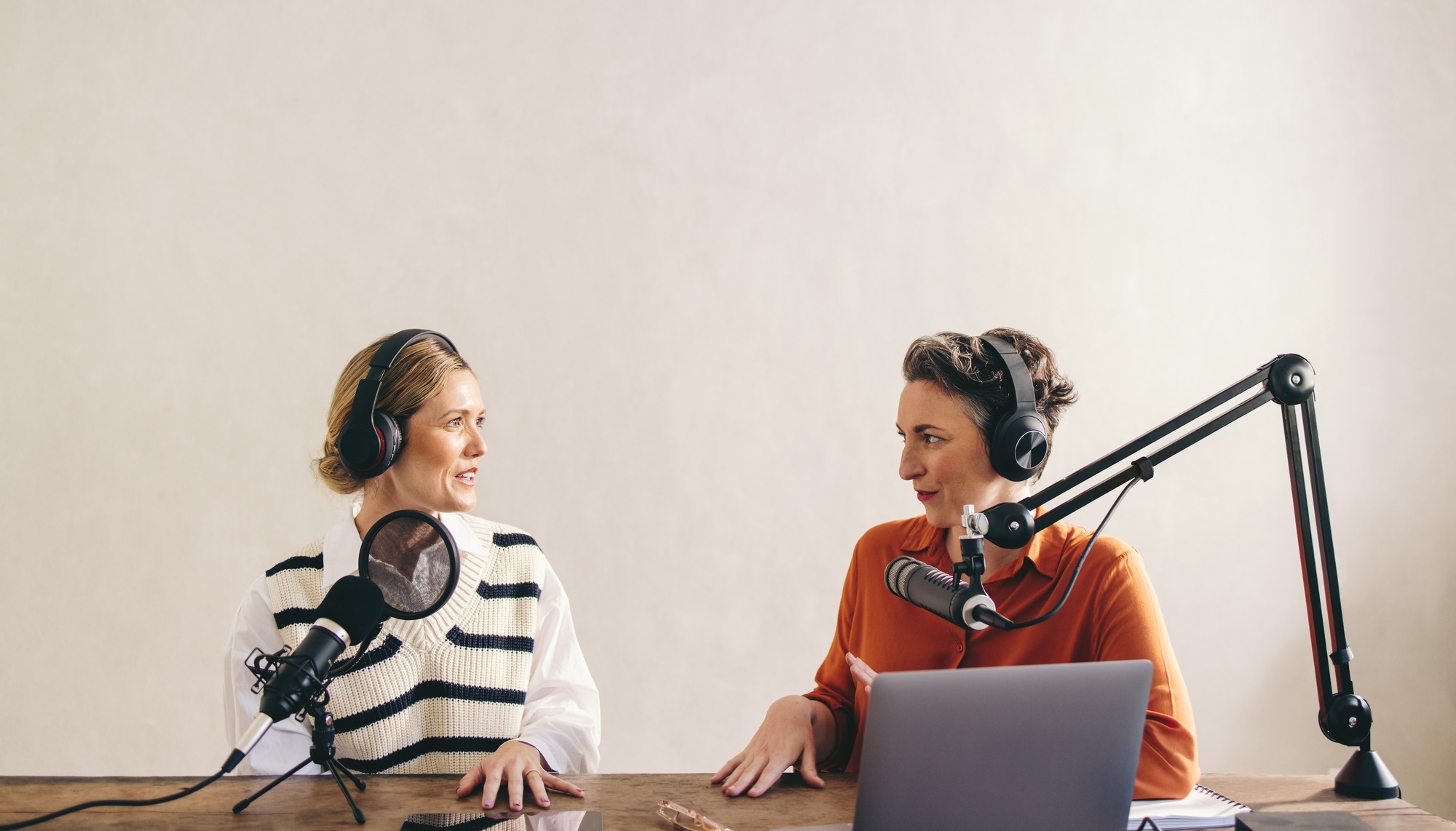 Two female podcasters having a conversation while co-hosting an a show in a home studio. Two women recording an audio broadcast for their social media channel.